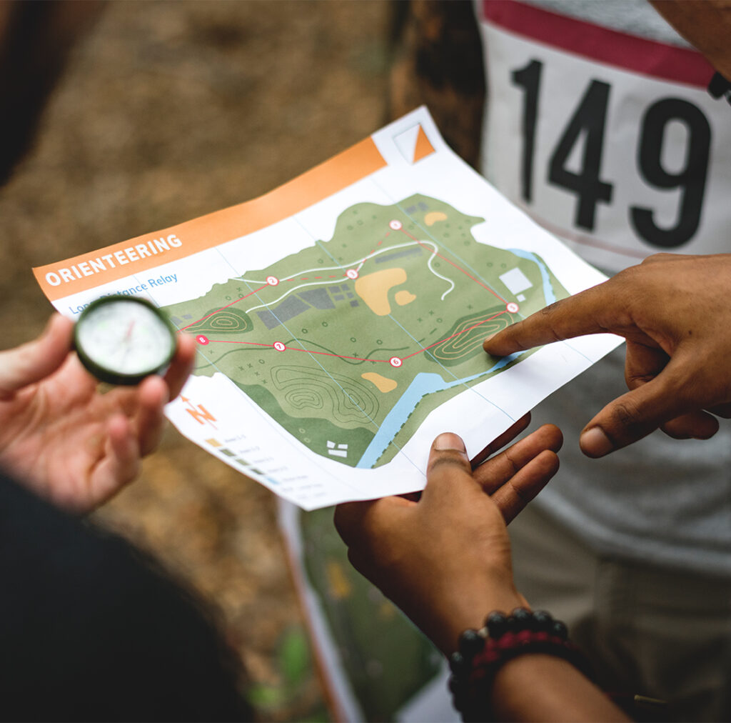 Close-up of people using strategy with a compass and orienteering map, race bib visible.