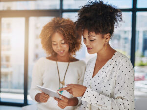 Two women in a bright, modern office review blog optimization tips together on a tablet.