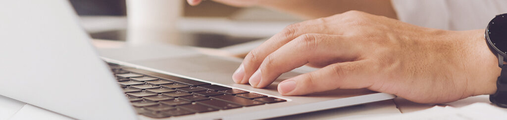 Close-up of a hand typing on a laptop keyboard, researching the benefits of local SEO.