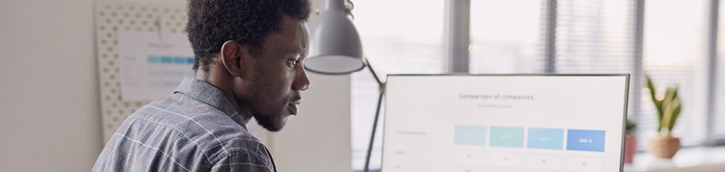 Man at a desk reviews a comparison table on his monitor, researching how to get blog traffic in a modern office.