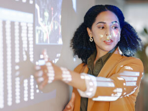 Woman in a tan blazer points at projected data on how AI will affect marketing during her presentation.