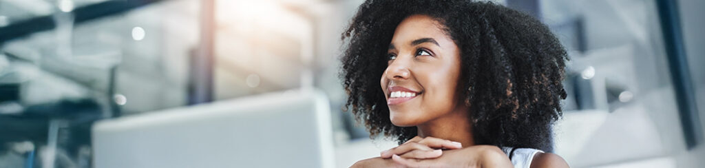 Woman with curly hair smiling while sitting at her desk, updating her Google profile for business.