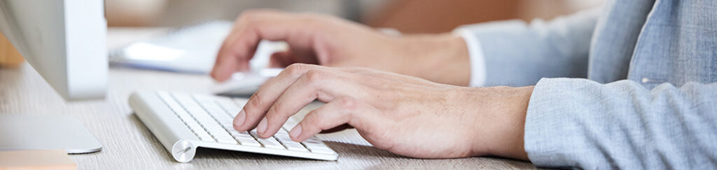 Person working on content strategy for a website, typing on a white keyboard with computer monitor partially visible.