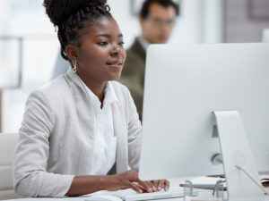 A woman in business attire works on a website redesign at her desktop computer in a modern office.