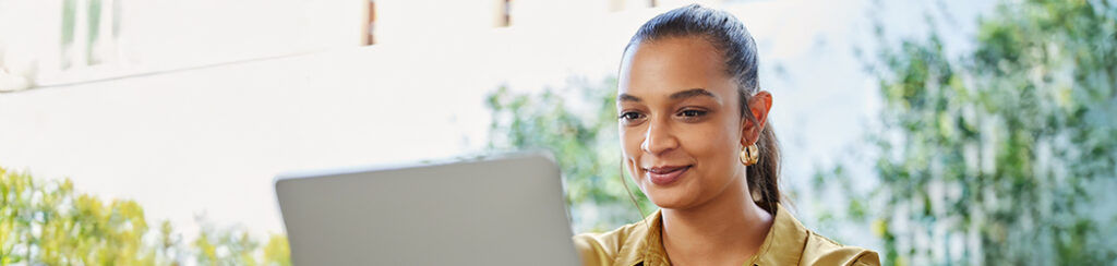 A woman sits outdoors, smiling at her laptop, exploring why content marketing important amid greenery and natural light.