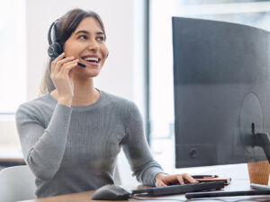 A woman wearing a headset smiles while discussing local SEO marketing services at her computer desk.