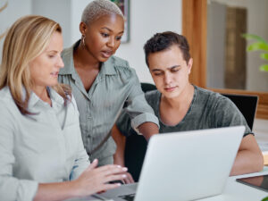 Three people discuss examples of AI in marketing around a laptop in a modern office setting.