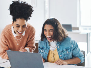 Two women discuss how to tell if marketing is working while viewing data on a laptop.