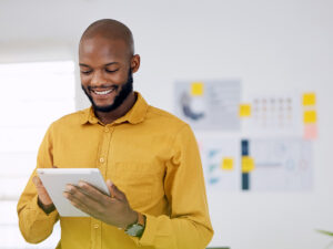 A man in a yellow shirt smiles while using a tablet to list his business on Google Maps.
