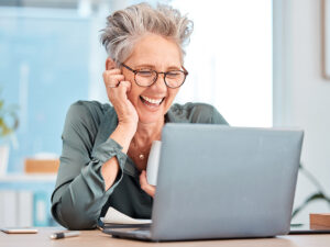 Smiling older woman uses a laptop to look up the importance of online presence for small businesses.