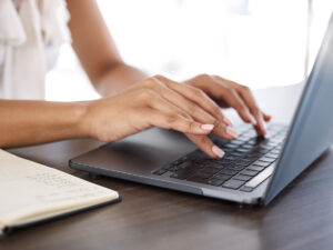 Close-up of a person typing on a laptop with an on page seo checklist on a notebook