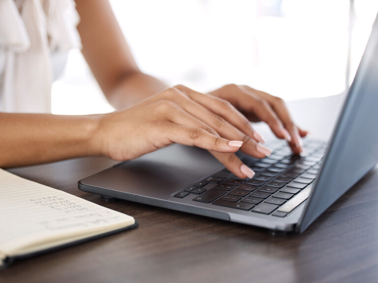 Close-up of a person typing on a laptop with an on page seo checklist on a notebook