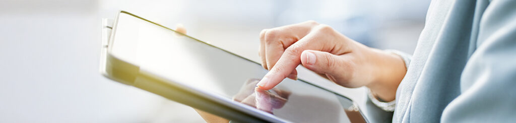 A person uses their index finger to touch the screen of a digital tablet, holding it with their other hand.