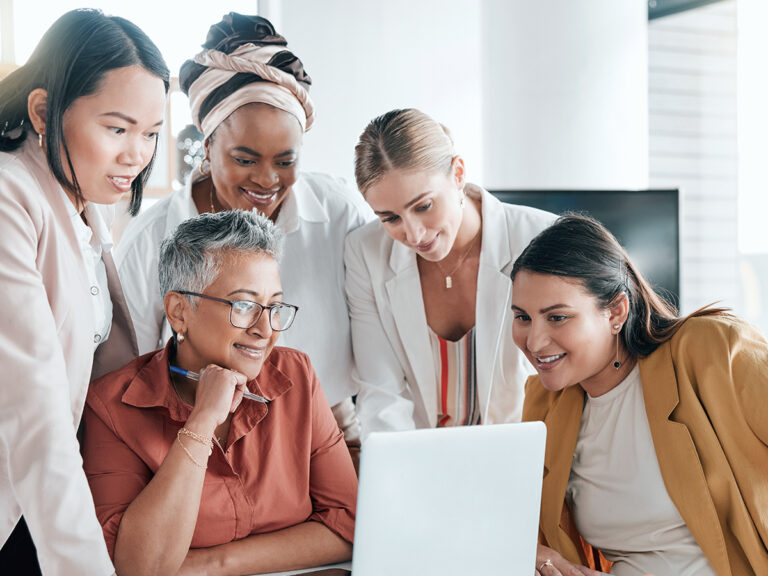 Five women collaborate around a laptop, strategizing on improving their website conversion funnel.