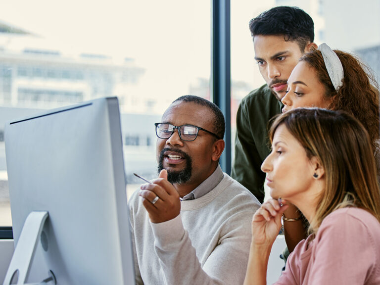 Four people in an office discuss a computer screen, collaborating on a customer acquisition strategy.