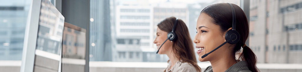 Two women wearing headsets work at computers, boosting website engagement.