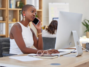 Woman in white sleeveless top using a computer to monitor website traffic while talking on her phone.