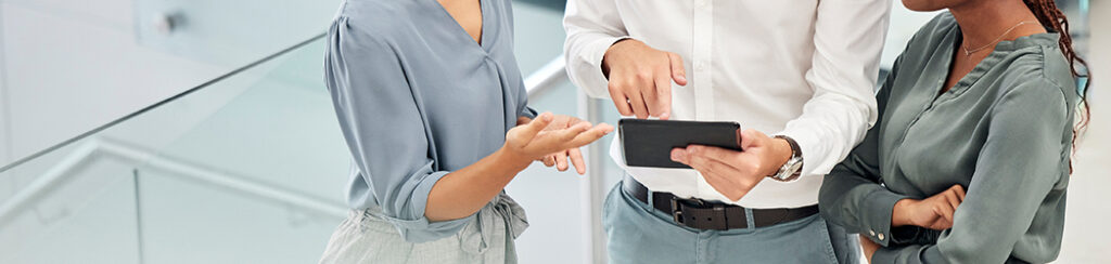 Three people stand together indoors, discussing local business ranking as they review information on a tablet.