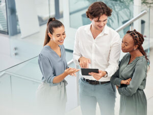 Three professionals stand indoors, discussing local business ranking insights displayed on a digital tablet.