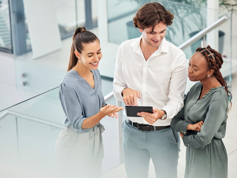 Three professionals stand indoors, discussing local business ranking insights displayed on a digital tablet.