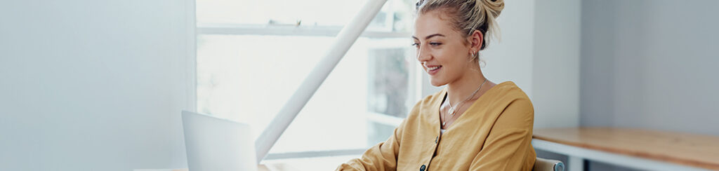Woman in a yellow shirt sits at a desk, updating her Google Business Profile on a laptop
