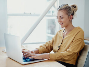 A woman smiles while typing on her laptop, ready to update Google Business Profile