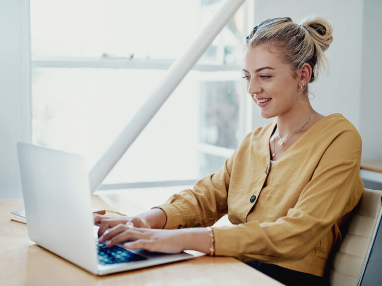 A woman smiles while typing on her laptop, ready to update Google Business Profile