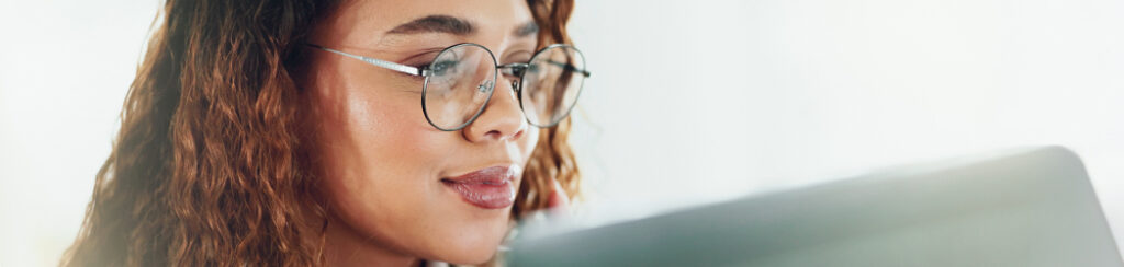 Woman with glasses and curly hair exploring how to use AI for marketing on her laptop in a bright setting.