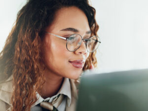 A person with curly hair and glasses looks at a laptop screen, focused on learning how to use AI for marketing.