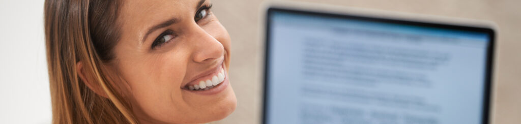 Woman smiling at the camera while sitting in front of a computer, ready to improve SEO with blogging.