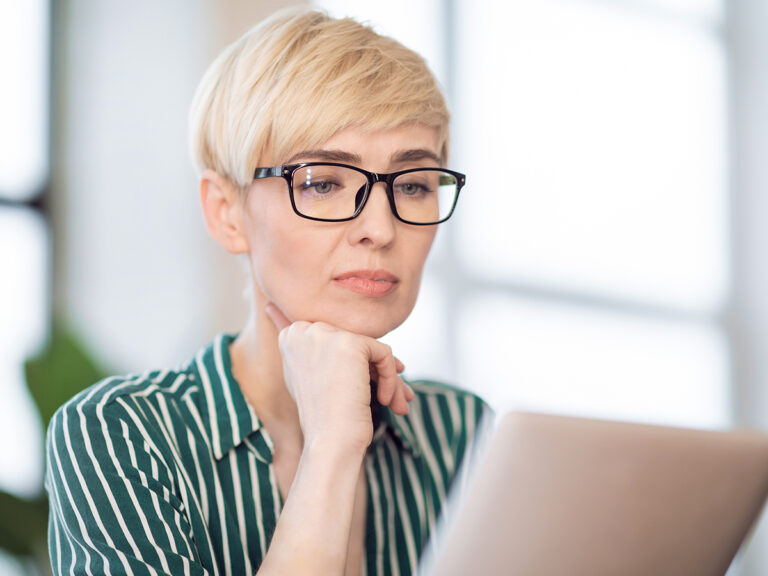 A person with short blonde hair and glasses studies service pages that convert on her laptop.