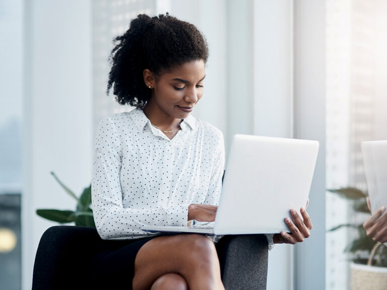 A woman in business attire works on a laptop, using a blog as a lead generation tool
