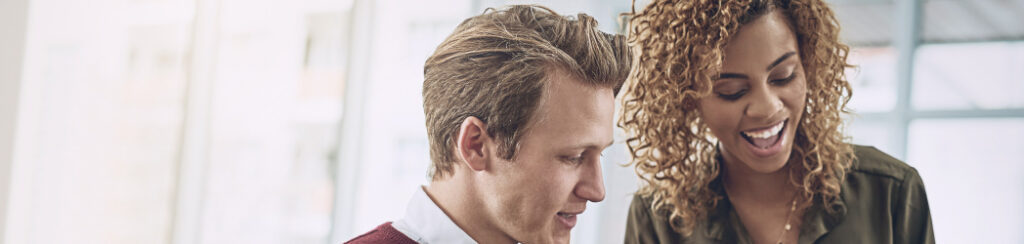 Two colleagues looking at documents together and smiling in a bright office setting.