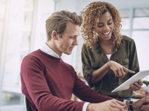 Two colleagues discussing something on a tablet in a bright office setting.