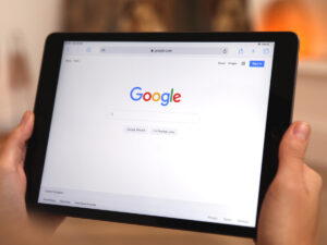 Person holding a tablet displaying the Google search homepage in a web browser.