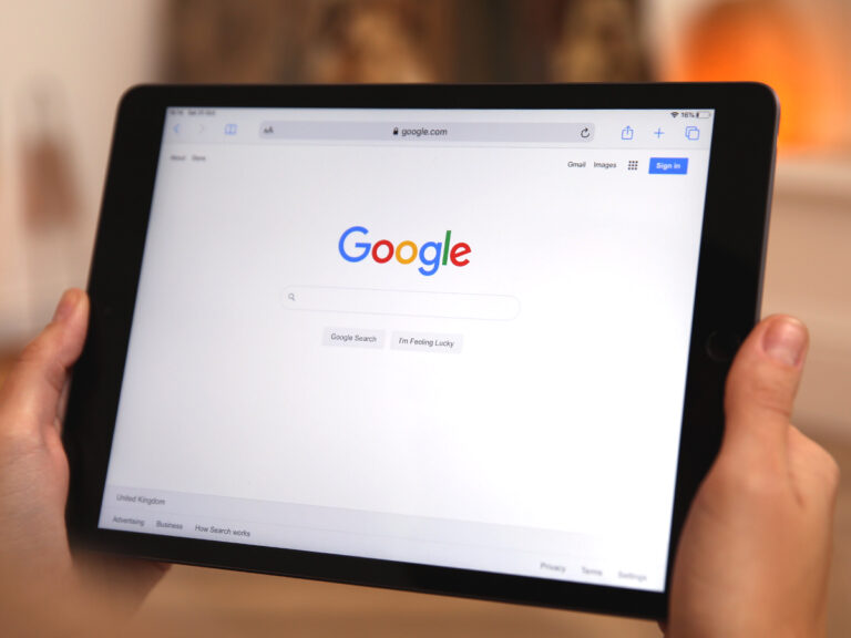 Person holding a tablet displaying the Google search homepage in a web browser.