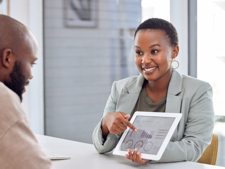 Woman showing a man a tablet displaying SEO and click through rate graphs during a business meeting at a desk.