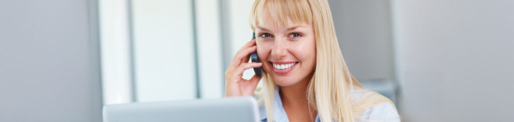 Smiling woman with long blonde hair talks on the phone at her desk while viewing a Google Business Profile page.