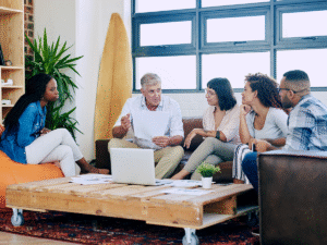 five employees discussing customer testimonials on a laptop during a team meeting