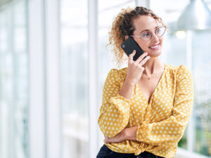 Woman in a yellow polka dot blouse smiles while talking on her smartphone, discussing high quality leads