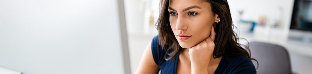 Woman with long dark hair looks intently at local search results on her computer screen in a bright room.
