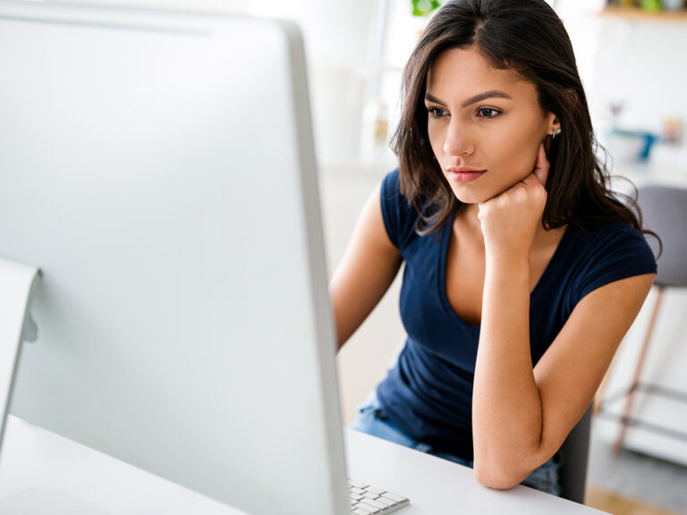 Woman sitting at a desk, looking at local search results on a computer monitor with her chin resting on her hand.