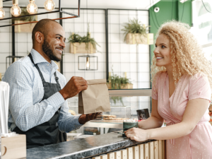 Smiling cafe owner hands a customer a takeout bag, a small business aiming to rank on Google Maps.